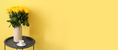 Sarı duvarın yanındaki masanın üzerinde güzel güller olan vazo. Tasarım için pankart