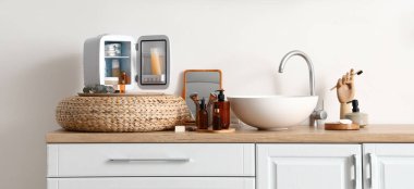 İçinde ürünler, ayna ve lavabo olan buzdolabı banyodaki ışık duvarının yanında.