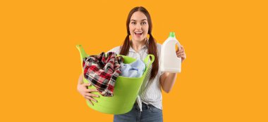 Sarı arka planda çamaşır ve deterjanı olan mutlu genç bir kadın.