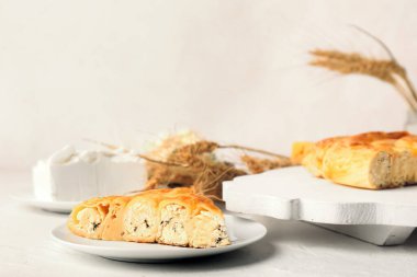 Lezzetli peynirli turta ve beyaz masada buğday kulaklı tabaklar.