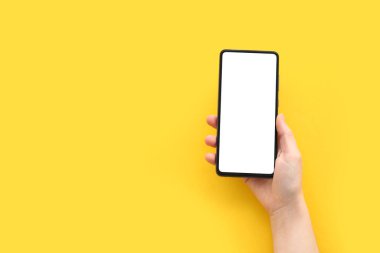 Female hand with modern mobile phone on yellow background