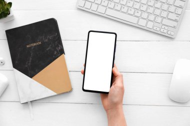 Female hand with modern mobile phone, computer mouse and keyboard on light wooden background