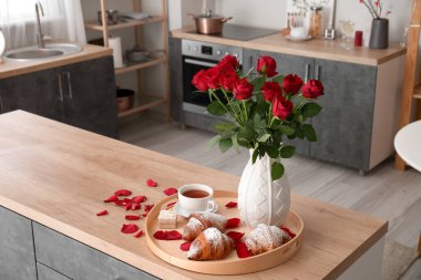 Engagement ring, cup of tea, croissants and vase with roses on counter in kitchen