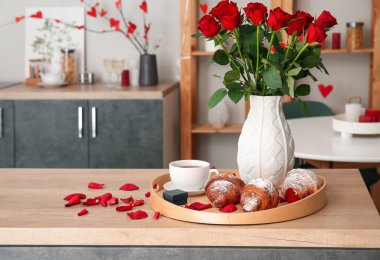 Engagement ring, cup of tea, croissants and vase with roses on counter in kitchen decorated for Valentine's Day