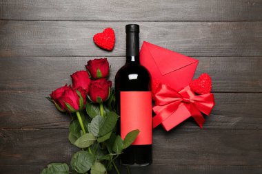 Red roses, envelope, bottle of wine and candles on dark wooden background. Valentine's Day celebration