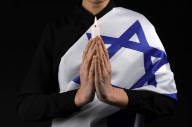 Young woman with candle and flag of Israel praying on black background, closeup. International Holocaust Remembrance Day