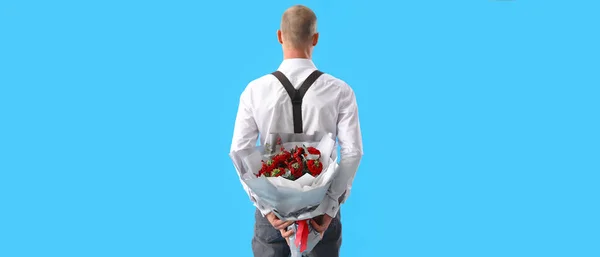 Young man with bouquet of flowers on blue background, back view. Valentine\'s Day celebration