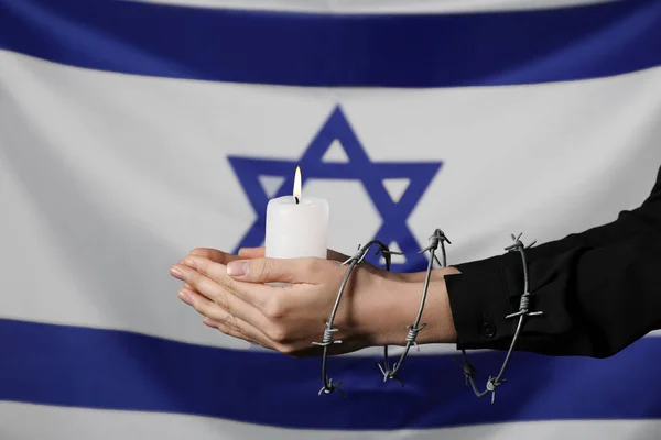 Woman with barbed wire and candle against flag of Israel. International Holocaust Remembrance Day