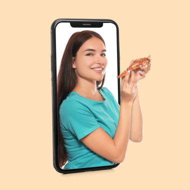 Woman with slice of fresh pizza looking out of phone screen on beige background