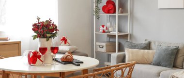 Interior of dining room with beautiful bouquet of flowers, glasses of wine and gift for Valentine's Day celebration