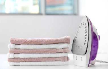 Elbise yığını ve elektrikli ütü masanın üstünde, yakın plan.