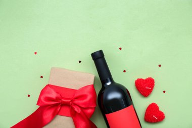 Hediyeli bir şişe şarap, mumlar ve yeşil arka planda kalpler. Sevgililer Günü kutlaması