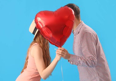 Mavi arka planda kalp şeklinde bir balonun arkasına saklanan mutlu genç çift. Sevgililer Günü kutlaması