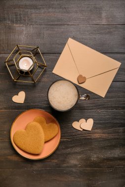 Bir fincan kahve, kurabiye, zarf, mum ve kalpler koyu ahşap arka planda. Sevgililer Günü kutlaması