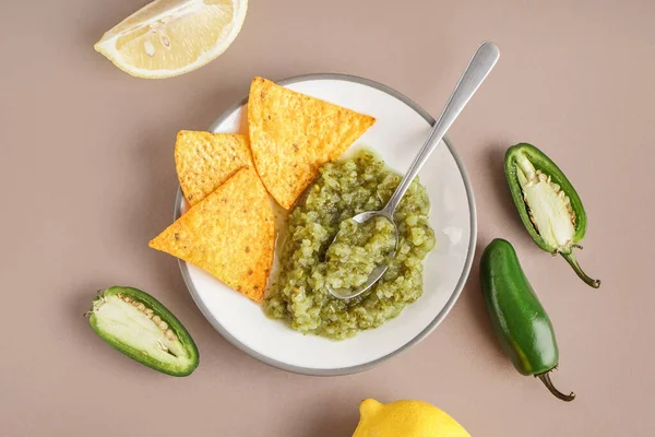 Plate of tasty green salsa sauce with nachos on color background