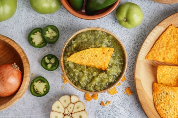 Bowl of tasty green salsa sauce with nacho on light background