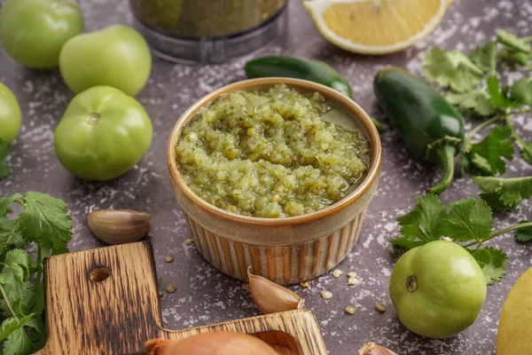 Bowl of tasty green salsa sauce and ingredients on grunge background