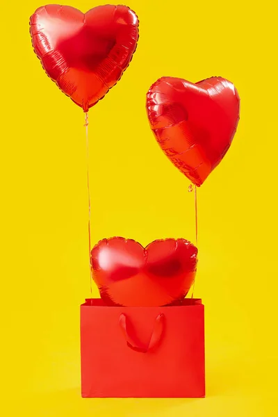 Shopping bag with heart-shaped balloons for Valentine\'s Day on yellow background