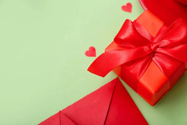 Gift with envelope and hearts on green background, closeup. Valentine\'s Day celebration