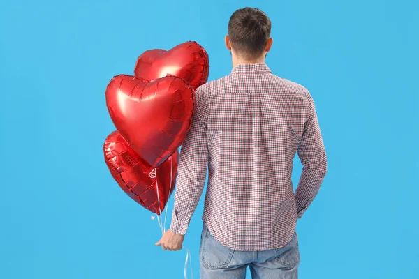 Handsome man with heart-shaped balloons on light blue background, back view. Valentine\'s Day celebration