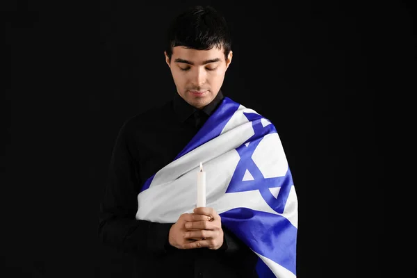Jewish man with candle and flag of Israel honoring victims of Holocaust on dark background
