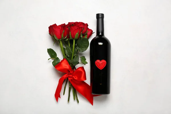 Red roses with bow and bottle of wine on white background. Valentine\'s Day celebration