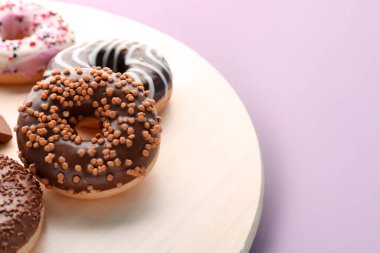 Wooden board with delicious donuts on color background, closeup