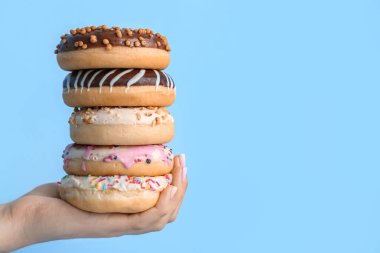 Female hand with stack of tasty donuts on color background, closeup