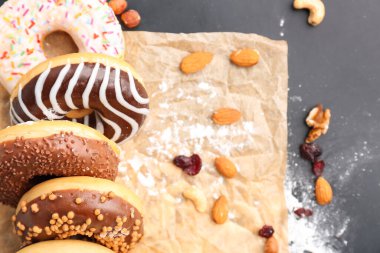 Sheet of baking paper with tasty donuts and nuts on dark background, closeup