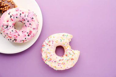 Plate with delicious donuts on lilac background