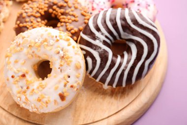Wooden board with delicious donuts on lilac background, closeup