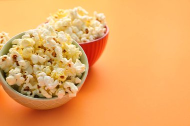 Bowls of delicious popcorn on color background