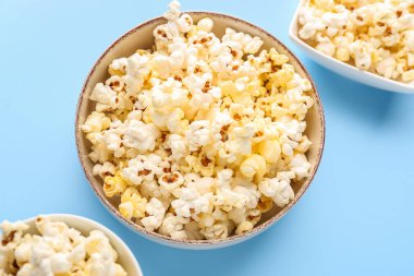 Bowls of delicious popcorn on color background, closeup