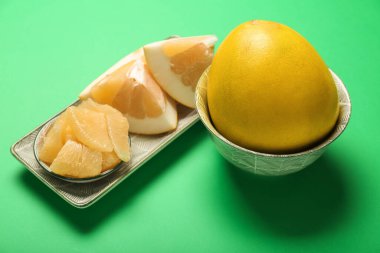 Plates with halves and slices of pomelo fruit on green background