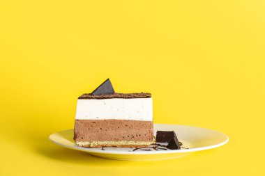 Plate with piece of birds milk cake and chocolate on yellow background