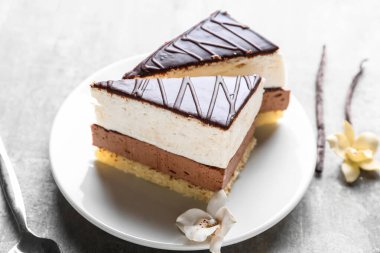 Plate with pieces of birds milk cake and vanilla on grey table