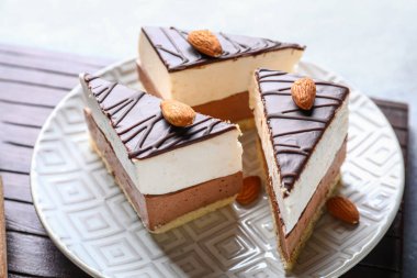 Board with plate of birds milk cake pieces and almond nuts on grey background