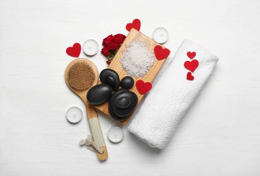 Beautiful spa composition for Valentine's Day with brush, stones, rose flowers, sea salt and candles on white wooden background