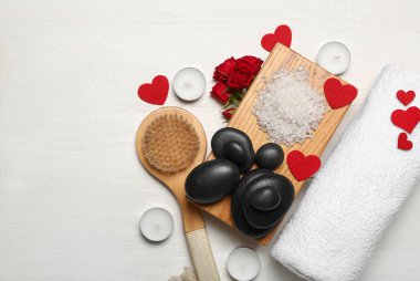 Beautiful spa composition for Valentine's Day with brush, stones, rose flowers, sea salt and candles on white wooden background