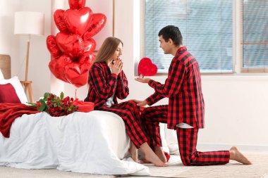 Genç bir adam sevgililer gününde yatak odasında kız arkadaşına evlenme teklif ediyor.