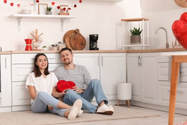 Happy couple with gift sitting in kitchen on Valentine's Day