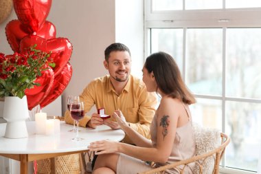 Young man proposing to his girlfriend in kitchen on Valentine's Day