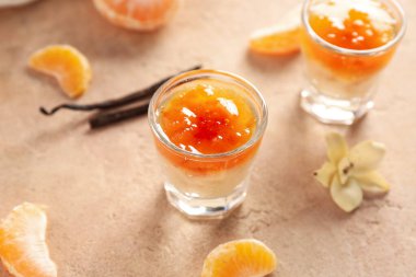 Shots of delicious pudding with jam, vanilla sticks and tangerine segments on beige table