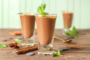 Shots of delicious chocolate pudding with cinnamon and mint on wooden table