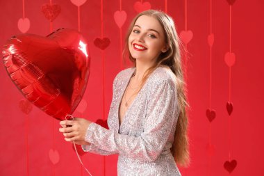 Beautiful young woman with heart-shaped balloon on red background. Valentine's Day celebration