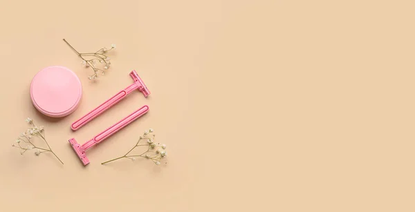 Razors for hair removing, jar of cosmetic cream and flowers on beige background with space for text