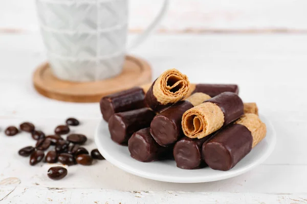 Plate with tasty wafer rolls, coffee beans and cup on light background