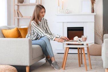 Young woman taking magazine from table at home