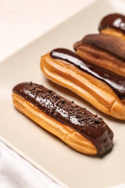 Plate with sweet chocolate eclairs on light background, closeup