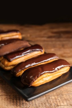 Plate with tasty chocolate eclairs on dark wooden table, closeup